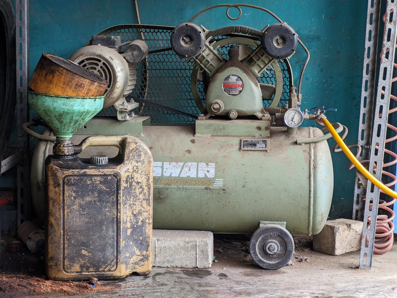 Old industrial air compressor and oil can in a rustic workshop setting. Ideal for industrial themes.